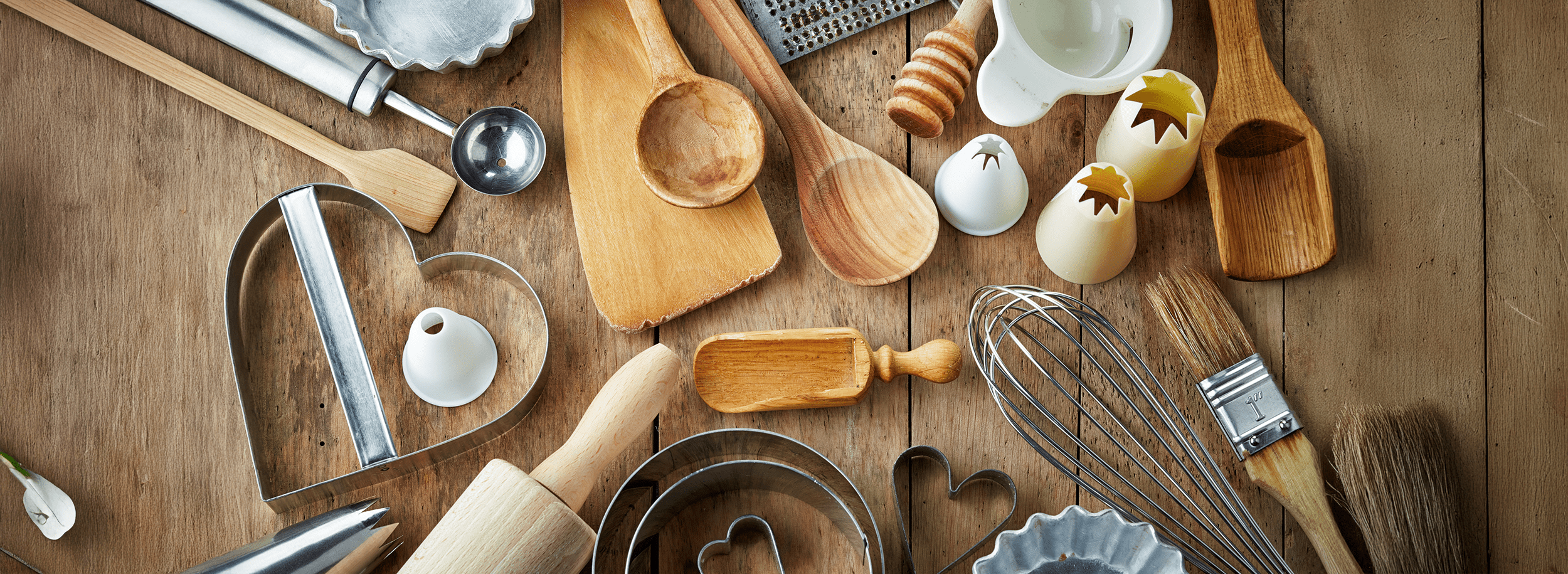 Assorted baking tools and utensils, including rolling pins, cookie cutters, and measuring spoons, arranged on a wooden surface.